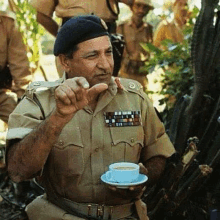 a man in a military uniform is holding a cup of coffee and a saucer .