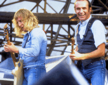 two men are playing guitars on a stage and one is smiling