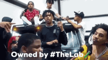 a group of young men are sitting on top of a car with the words owned by # thelab written on the bottom .