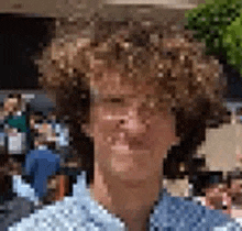 a man with curly hair and a blue shirt is standing in front of a crowd of people .