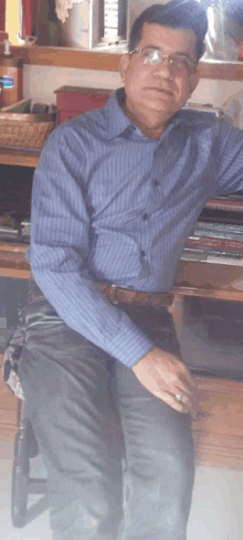 a man wearing glasses and a blue shirt stands in front of a shelf with books on it