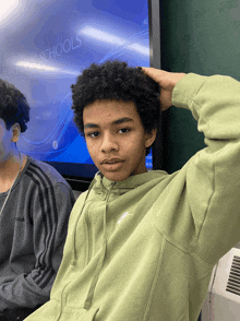 a young man in a green nike hoodie sits in front of a screen that says advanced schools