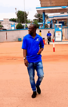 a man wearing a blue shirt that says ' mercedes benz ' on it walks in front of a gas station