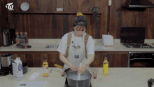 a woman in an apron stirs a pot of liquid in a kitchen with twice beauty tv on the shelf above her