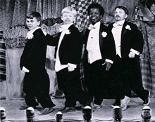 a group of men in tuxedos and bow ties are dancing on a stage