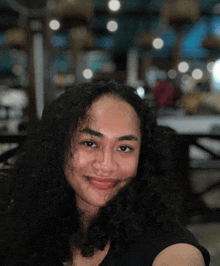 a woman with curly hair and a black shirt smiles for the camera