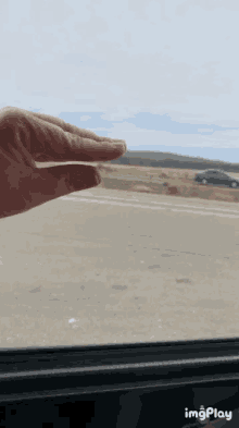 a person 's hand is reaching out of a car window and a car is in the background