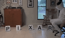 a man in a white shirt is sitting in a chair with pixar letters on the floor in front of him