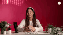 a woman in a white sweater is sitting at a desk in front of a red background with a foreign language written on it