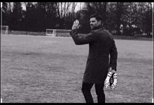 a man in a trench coat holds a pair of soccer cleats in his hand