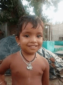 a young boy without a shirt is wearing a necklace and smiling for the camera .