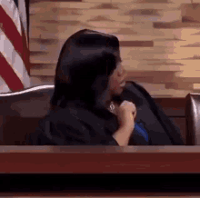 a woman in a judge 's robe is sitting at a table in a courtroom with her hands folded .