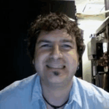 a man with curly hair is smiling for the camera while wearing a blue shirt and a necklace .