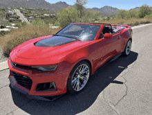 a red sports car with a convertible top is parked on a road with mountains in the background