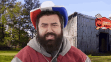 a man with a beard wears a red white and blue hat in front of a sign for brand 's bbq