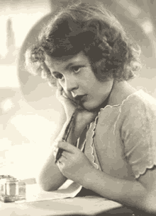 a young girl is sitting at a table holding a pen .