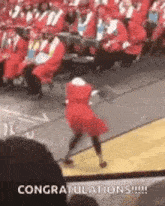 a woman in a red dress is dancing in front of a crowd of graduates at a graduation ceremony .