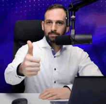 a man in a white shirt is giving a thumbs up in front of a microphone