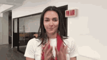 a woman wearing a white shirt and a red scarf is clapping her hands in front of a sign that says on air .