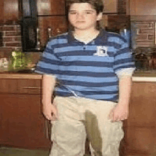 a boy in a blue and white striped shirt is standing in a kitchen with a stain on his pants