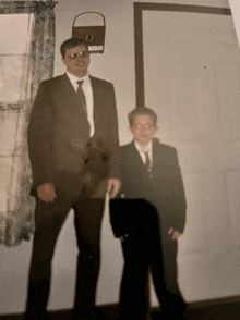 a man in a suit stands next to a boy in a suit and tie