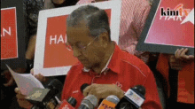 a man in a red shirt is holding a piece of paper in front of a group of people holding signs that say hain