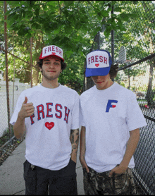 a man wearing a fresh life shirt stands next to another man wearing a blue fresh hat