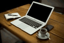 a laptop is sitting on a wooden table next to a cup of coffee .