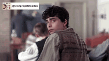 a young man with curly hair is looking over his shoulder at the camera while sitting in a classroom .