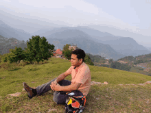 a man sits on a grassy hillside with mountains in the background