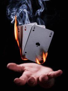 a hand holding a stack of aces on fire