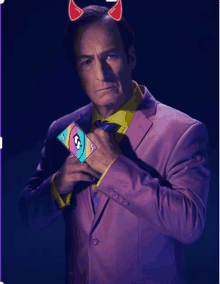 a man in a purple suit and tie is holding a card with a devil horn on it