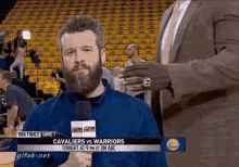 a man with a beard is holding a microphone in front of a screen that says cavaliers vs warriors on it