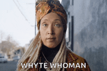 a woman with dreadlocks and a turban is standing in front of a building and says whyte whoman .