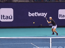 a tennis player is swinging a racket at a ball on a court with a betting advertisement in the background