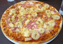 a pizza with bananas , ham , pineapple and cheese is on a white plate on a table .