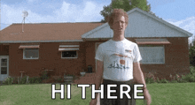 a man in a white shirt is standing in front of a brick house with the words hi there above him .