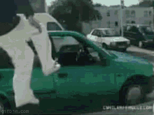 a person is jumping into a green car with their legs out the window .