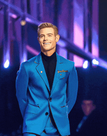 a man wearing a blue suit and black turtleneck smiles