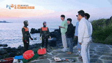 a group of people standing on a rocky shoreline with a sign above them that says ' 1 / 2 / '