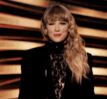 taylor swift is wearing a black lace top and a black jacket while standing on a stage .