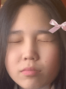 a close up of a girl 's face with her eyes closed and a pink bow on her forehead .