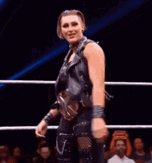 a woman is standing in a wrestling ring wearing a leather vest and choker .