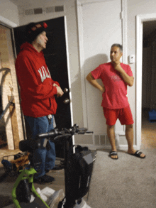 a man in a red hoodie that says ' xmas ' on it stands next to a man in a pink shirt