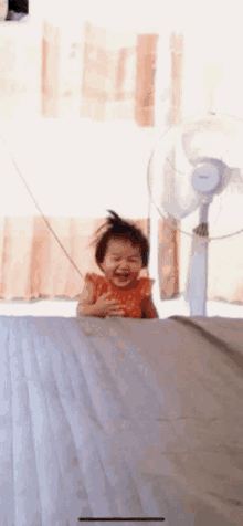 a little girl is sitting in front of a fan