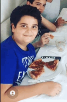 a boy in a blue shirt is eating pizza