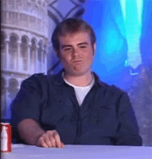 a man in a blue shirt is sitting at a table with a can of soda in front of him