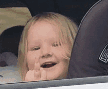 a little girl is giving the middle finger in a car seat .