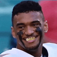 a football player with black paint on his face is smiling and wearing gold grills .