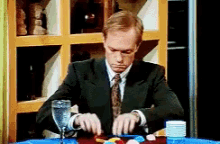 a man in a suit and tie is sitting at a table with a glass of water in front of him